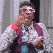 a man wearing sunglasses and a purple scarf is holding a wallet and laughing .