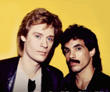a man with a mustache stands next to another man with blonde hair