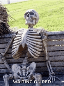 a skeleton is sitting on a wooden bench with the words " waiting on red " above it