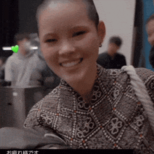 a woman with a shaved head is smiling and wearing a patterned shirt with flowers on it