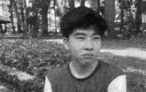 a black and white photo of a boy in a park with trees in the background