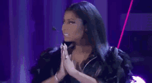 a woman is standing in front of a purple curtain with her hands folded in front of her face .