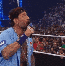 a man in a blue shirt with the letter m on it is standing in a wrestling ring .