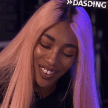 a woman with pink hair is smiling with her eyes closed and a sign above her head that says dasding