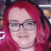 a woman with pink hair wearing glasses and a choker is smiling
