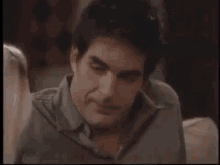 a man in a grey shirt is sitting on a couch and looking at something .