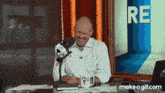 a man sitting in front of a microphone with the word re on the wall behind him