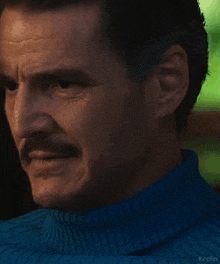 a close up of a man with a mustache wearing a blue sweater .