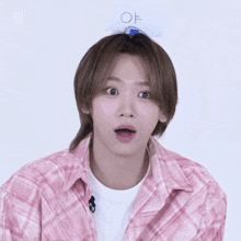 a young man wearing a pink plaid shirt has a sign on his head that says ' of '