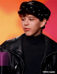a young man wearing a black hat and a black jacket
