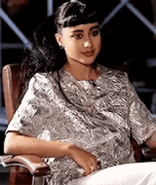 a woman is sitting in a chair wearing a floral shirt .