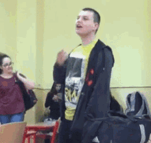 a man in a yellow shirt is standing in a classroom with his hands up .