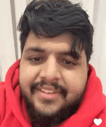 a man with a beard is smiling and wearing a red hoodie .