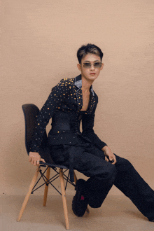 a man in a black suit sits on a chair wearing sunglasses