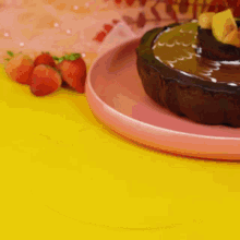 a chocolate cake on a pink plate next to strawberries on a yellow table