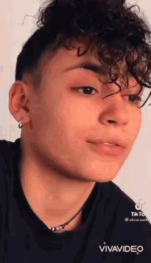 a close up of a young man with curly hair wearing a black shirt and earrings .