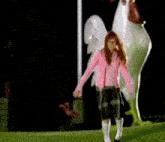 a girl in a pink jacket and plaid skirt is dancing in front of a chicken statue .