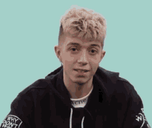 a young man with blonde hair is wearing a black hoodie and a white shirt .