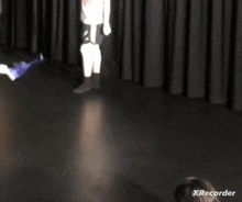 a person is crawling on the floor in front of a black curtain with xrecorder on the bottom right