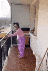 a woman in purple pajamas is standing on a balcony holding onto a railing .