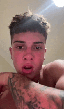 a shirtless young man with a tattoo on his arm is talking to the camera .