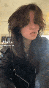 a woman with long hair and a nose ring is wearing a black leather jacket .