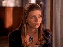 a woman wearing a blue lace top and a necklace looks at the camera