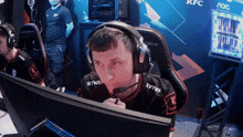 a man wearing headphones and a shirt that says syner sits in front of a monitor