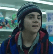 a young boy wearing a hat and a blue jacket is standing in front of a store shelf .