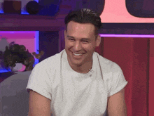 a man wearing a white shirt is smiling in front of a red wall