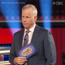 a man in a suit is holding a family feud canada sign