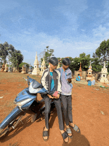 two boys are sitting on a blue motorcycle looking at their cell phones