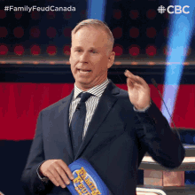 a man in a suit and tie is holding a family feud board