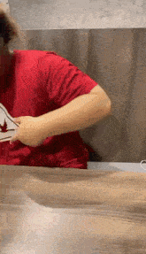 a man in a red t-shirt is sitting at a table holding a piece of paper .