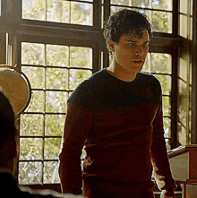 a man in a red and black sweater is standing in front of a window with a globe in the background .