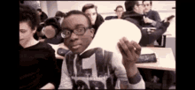 a man with glasses is holding a light bulb in a classroom .