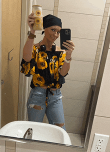a woman in a sunflower shirt is taking a selfie in a bathroom mirror