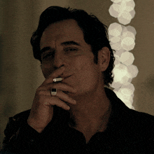 a man smoking a cigarette with a black ring on his finger