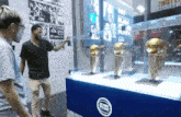 two men are looking at trophies in a glass case that says detroit pistons