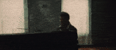 a man is playing a piano in front of a window in a dark room