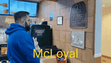 a man in a blue hoodie stands in front of a mcdonald 's counter with the words mcloyal on the wall