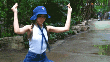 a girl wearing a blue hat and a white tank top is dancing in front of a sign that says change