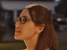 a woman wearing glasses and earrings looks to the left