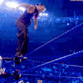 a wrestler in a black tank top is jumping over ropes