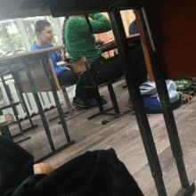 a boy in a blue shirt sits at a desk with a girl in a green shirt behind him