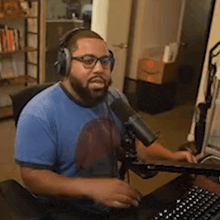 a man with a beard is wearing headphones and a microphone while sitting at a desk with a keyboard .