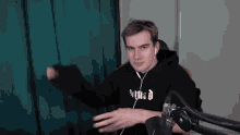 a man wearing headphones and a hoodie is sitting in front of a microphone .