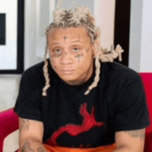a man with dreadlocks is sitting on a red couch wearing a black t-shirt .