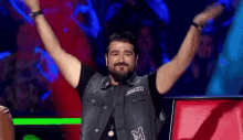 a man with a beard and a vest with the letter m on it is raising his arms in the air .