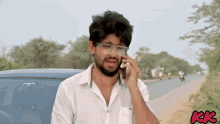 a man wearing glasses is talking on a cell phone in front of a car